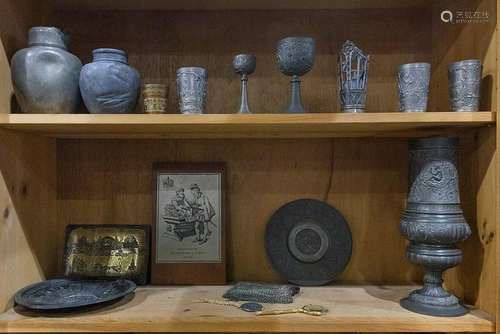 Two shelves of pewter table articles, including