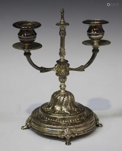 An Egyptian silver twin-branch candelabrum, raised on a domed foliate decorated circular base and
