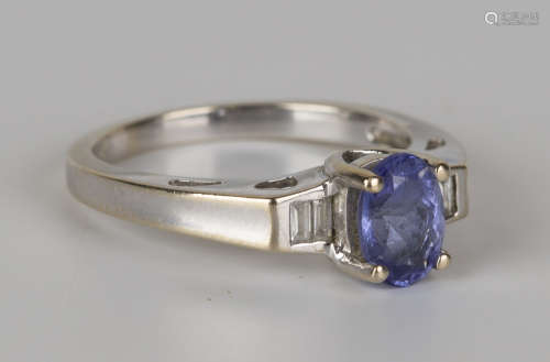 A white gold, blue gemstone and diamond ring, claw set with the oval cut blue gemstone between two