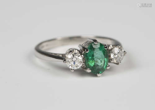 A platinum, emerald and diamond ring, claw set with an oval cut emerald between circular cut diamond