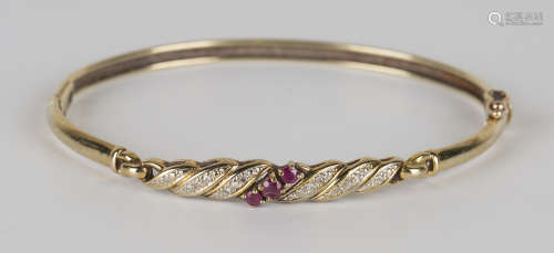 A 9ct gold, ruby and diamond oval hinged bangle, claw set with a row of three circular cut rubies
