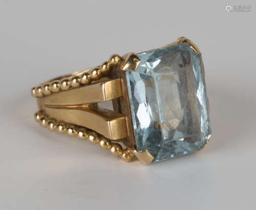 A gold ring, claw set with a cut cornered rectangular mixed cut aquamarine between beaded 'V' shaped