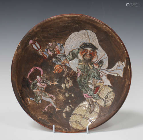 A Japanese earthenware circular dish, Meiji period, enamelled with a scene of Daikoku dancing upon