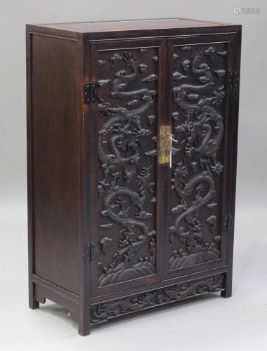 A Chinese hardwood two-door cabinet, early 20th century, each hinged rectangular door carved in
