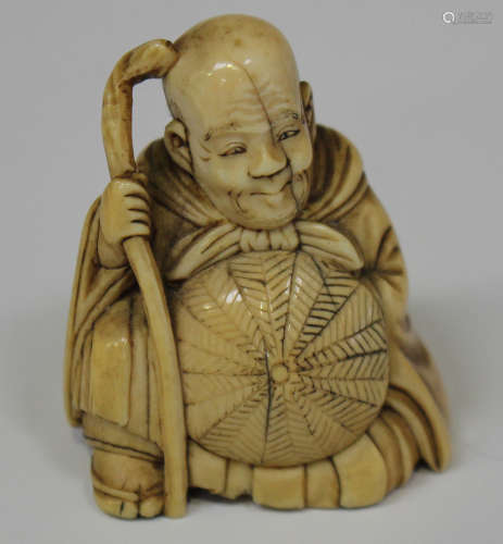 A Japanese carved ivory netsuke, Meiji period, modelled as a seated man wearing a long robe and