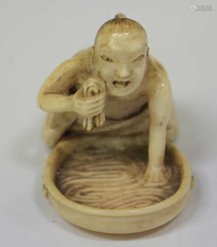 A Japanese carved ivory netsuke, Meiji period, modelled as a man kneeling over a shallow bowl of