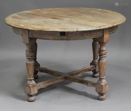 An early 20th century bleached oak extending circular dining table, the moulded top with two folding