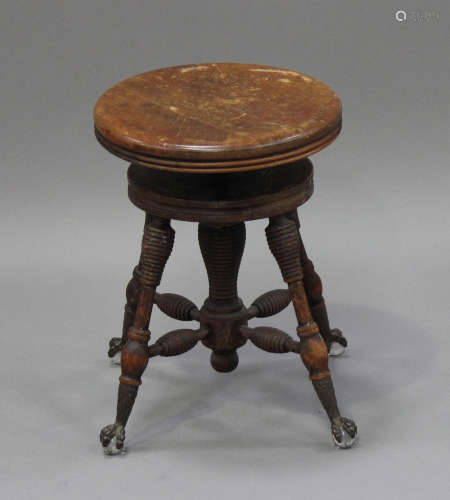 A late 19th century American walnut revolving piano stool, the ring turned legs terminating in