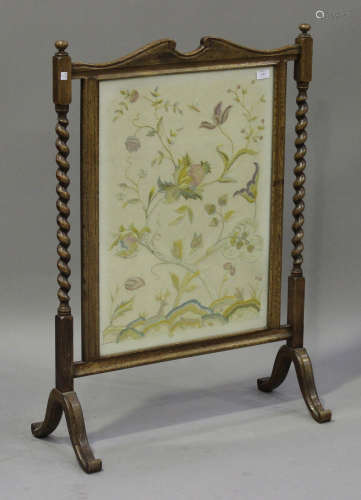 An early 20th century oak framed firescreen, inset with a floral needlework panel, on scroll feet,