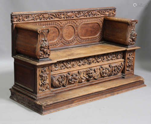 A 19th century Continental oak hall bench profusely carved with masks and floral scrolls, the