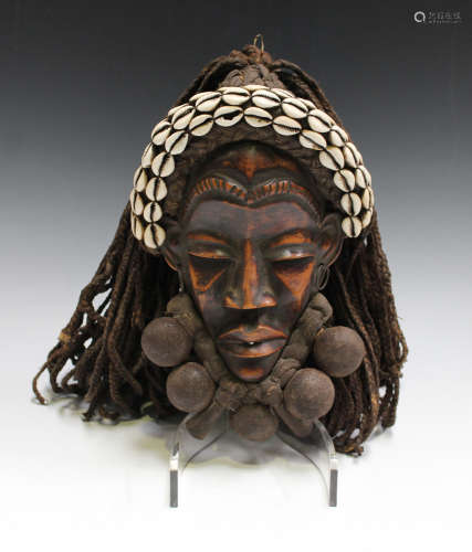 A Dan carved and stained wooden mask, Ivory Coast, with applied cowrie shells and woven string