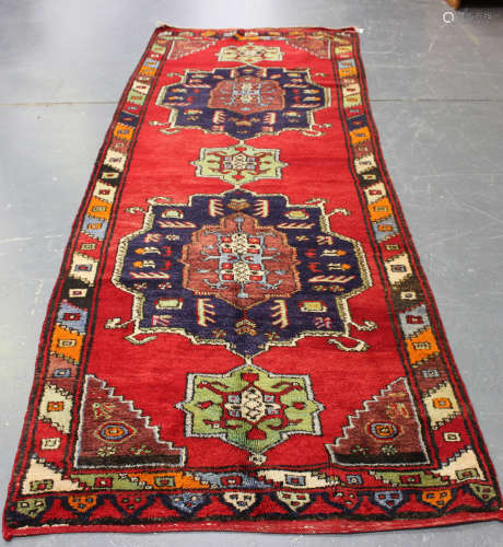 A Turkish runner, 20th century, the deep red field with two bold medallions, within a polychrome