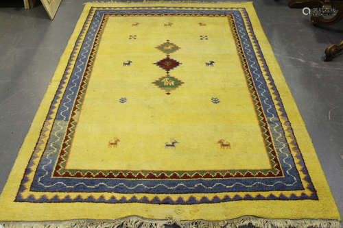 A Persian gabbeh rug, late 20th century, the sparsely decorated yellow field within a blue border,