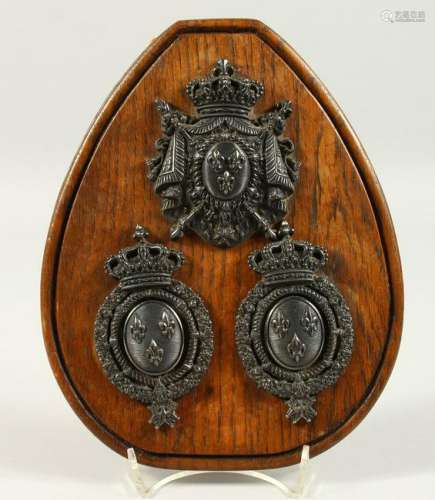 THREE CAST METAL ARMORIAL CRESTS, on an oak plaque.