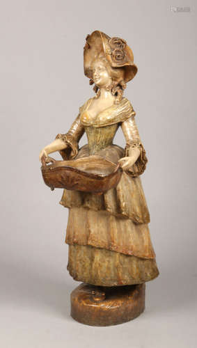 A large Goldscheider terracotta figure of a lady carrying a basket wearing a bonnet and a long