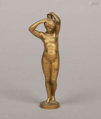 An Art Deco gilt bronze figure of a naked maiden stood and tending to her hair, raised on a small