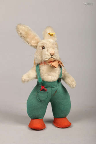 A Steiff Original mo hair rabbit. Wearing a bow tie, with green felt dungarees and orange shoes,