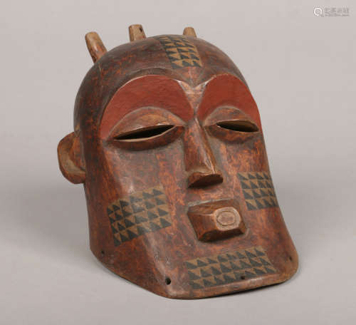 A West African carved hardwood tribal helmet mask. With painted detail and chevron banding, 25cm