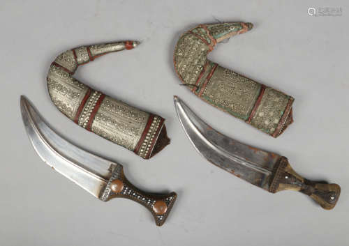 Two eastern Janbiya daggers with horn grips and white metal mounted scabbards.