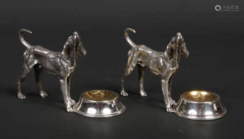 A pair of novelty cast white metal salt sellers. Each formed as a standing hound beside a large bowl