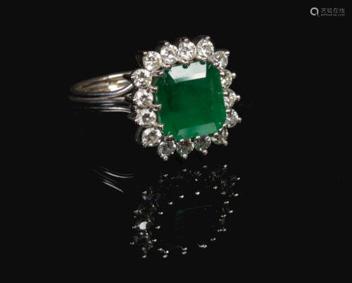An 18 carat white gold emerald and diamond cluster ring. Set with a large square step cut emerald