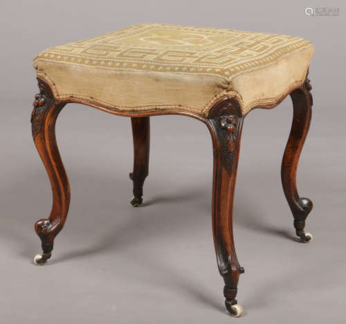 A Victorian carved walnut stool. With woolwork overstuffed seat and raised on scroll supports.