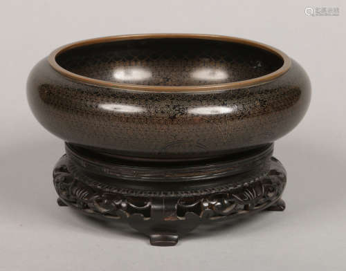 A Japanese cloisonne black ground bowl with wirework decoration and raised on a carved hardwood