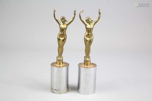 A Pair of Brass Feminine Nude Car Mascots, depicted standing with arms raised, on chrome plated plinths, approx 16 cms h