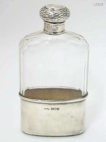 A glass hip flask with silver top and beaker to lower