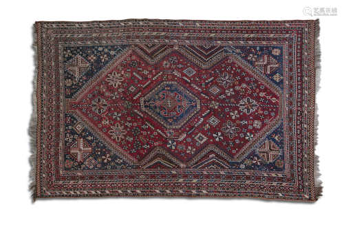 AN ANTIQUE TURKISH RED GROUND WOOL CARPET, woven in red, cream and navy blue tones, the centre field