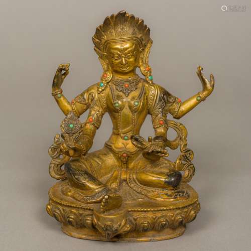 A gilt bronze model of a Tibetan four-armed deity Set with small coral and turquoise cabochons,