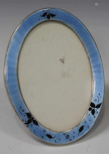 A George V silver, blue and black enamelled oval photograph frame, decorated with scattered leaves