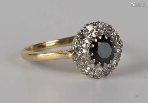 An 18ct gold, sapphire and diamond cluster ring, claw set with the circular cut sapphire within a