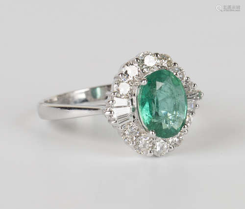 An 18ct white gold, emerald and diamond ring, claw set with an oval cut emerald within a surround of