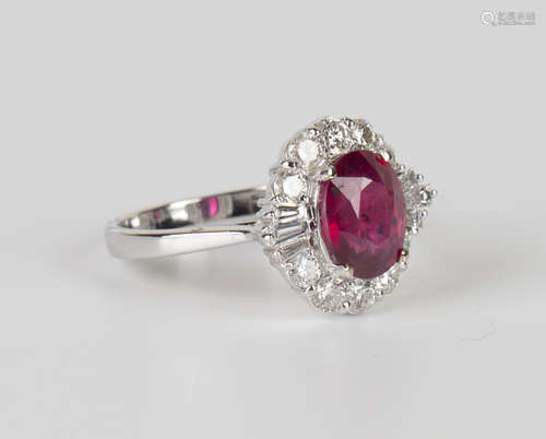 An 18ct white gold, ruby and diamond ring, claw set with an oval cut ruby within a surround of