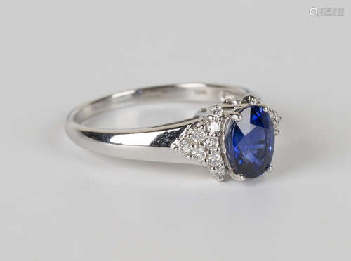 An 18ct white gold, sapphire and diamond ring, claw set with the oval cut sapphire between diamond