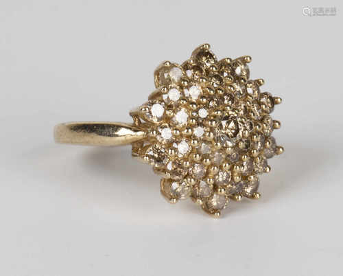 A 9ct gold and diamond cluster ring in a shaped circular design, mounted with circular cut champagne