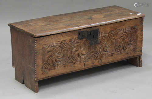 A 17th century elm six plank coffer, the hinged lid above a carved panel front, on shaped ends,