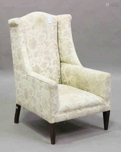 An Edwardian wing back armchair, the shaped back and arms upholstered in floral fabric, on square