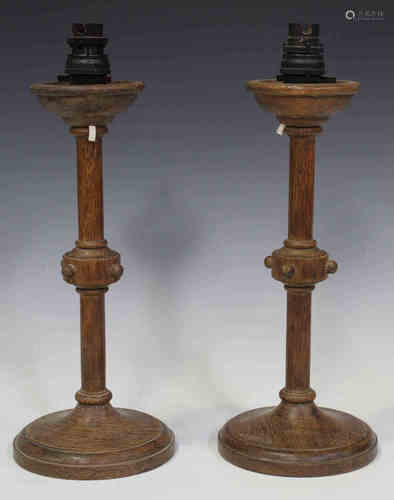 A pair of early 20th century Arts and Crafts style oak table lamps, the stems with beaded knops,