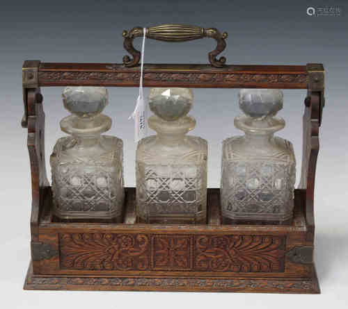 An Edwardian oak and plate mounted three-bottle tantalus, the three cut glass decanters held