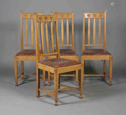 A set of four Edwardian Arts and Crafts oak framed dining chairs, each top rail finely carved with
