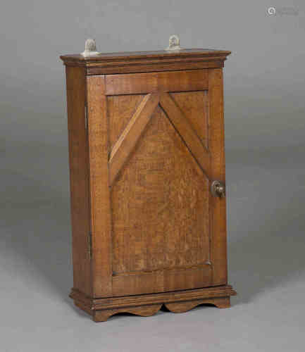 An Edwardian Arts and Crafts oak hanging wall cabinet, the bowed door with moulded panelling and