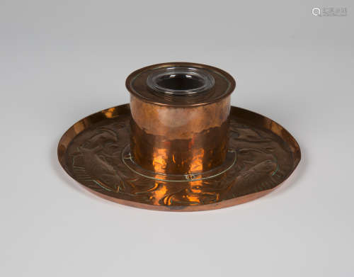 An Arts and Crafts Newlyn copper inkwell, the circular base worked with a band of fish, seaweed