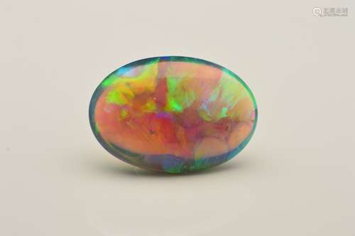 AN OVAL CABOCHON BLACK OPAL, showing flashes of electric blues, greens, orange and yellow colours,