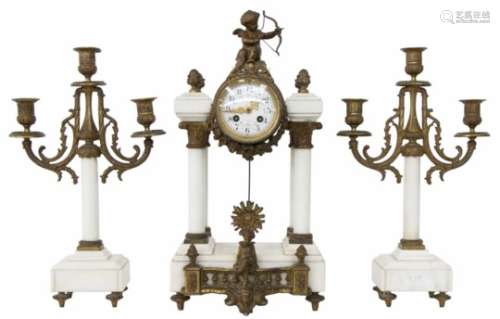 Een drie-delig witmarmeren klokkenstel bestaande uit een pendule en twee kandelaren. Versierd met