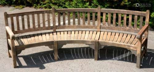 A CURVED TEAK GARDEN SEAT with slightly dished, slatted seat, 99cm h, 300cm l++Weathered but