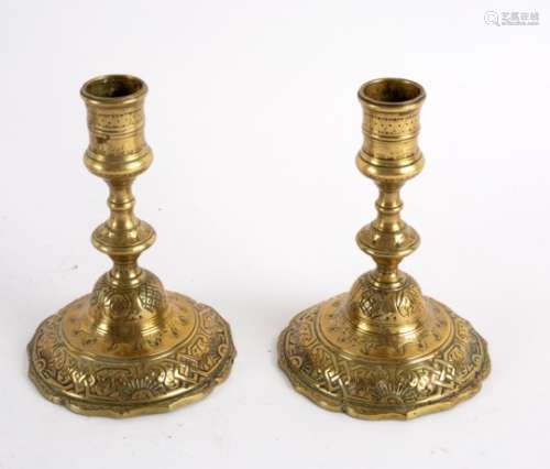 A pair of engraved brass candlesticks on skirt bases, 14.