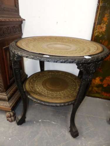 AN EASTERN CARVED EBONY TWO TIER STAND WITH BRASS TRAYS. Dia.70 x H.69cms.