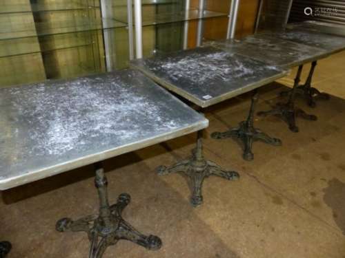 A SET OF FOUR VINTAGE CAFE TABLES WITH CAST IRON BASES EACH WITH ZINC WRAPPED TOPS.